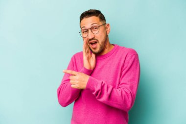 Genç İspanyol bir adam mavi arka planda izole edilmiş. Dedikodu yapıyor, bir şeyleri bildiriyor..