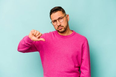 Genç İspanyol bir adam mavi arka planda izole edilmiş. Hoşlanmadığı bir hareket gösteriyor. Anlaşmazlık konsepti.