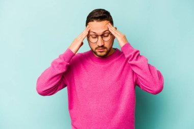 Genç İspanyol adam mavi arka planda izole edilmiş tapınaklara dokunuyor ve baş ağrısı çekiyor..