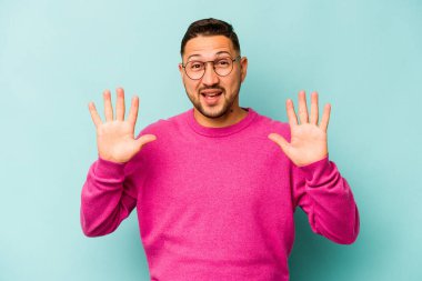 Genç İspanyol bir adam mavi arka planda izole edilmiş. Hoş bir sürpriz bekliyor. Heyecanlı ve el kaldırıyor..