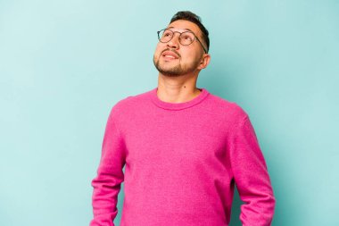 Mavi arka planda izole edilmiş genç bir İspanyol. Rahatlamış ve mutlu bir şekilde gülüyor. Boynunda dişler var..