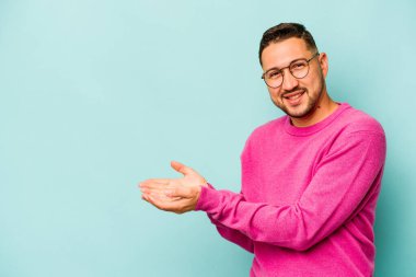 Mavi arka planda izole edilmiş genç İspanyol bir adam avucunun içinde bir kopyasını tutuyor..