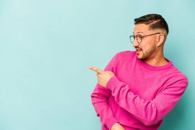 Genç İspanyol adam mavi arka planda izole edilmiş başparmak uzakta, gülüyor ve kaygısız.