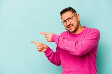 Mavi arka planda izole edilmiş genç bir İspanyol işaret parmaklarıyla işaret ederek heyecanlanıyor..