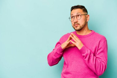 Latin kökenli genç bir adam mavi arka planda izole edildi. Aklında bir plan kuruyor, bir fikir kuruyor..