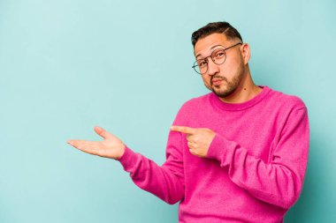 Mavi arka planda izole edilmiş genç İspanyol bir adam heyecanlı bir şekilde avuç içinde bir kopyasını tutuyor..