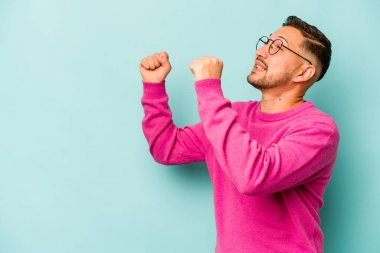 Mavi arka planda izole edilmiş genç İspanyol bir adam zaferden sonra yumruk kaldırıyor, kazanan konsept..