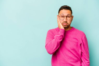 Mavi arka planda izole edilmiş, üzgün ve dalgın hisseden genç bir İspanyol fotokopi odasına bakıyor..