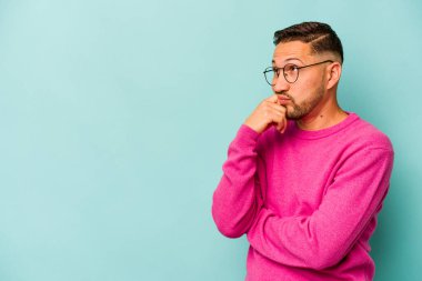 Mavi arka planda izole olmuş genç İspanyol bir adam rahatlamış bir şeyin fotokopi odasına baktığını düşünüyor..