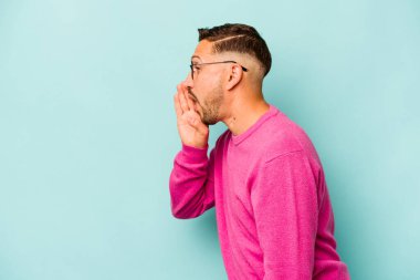 Mavi arka planda izole edilmiş genç İspanyol bir adam gizli bir sıcak fren haberi veriyor ve yana bakıyor.