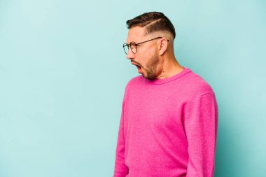 Genç İspanyol adam mavi arka planda izole edilmiş çok kızgın, öfkeli, hayal kırıklığına uğramış bağırıyor..