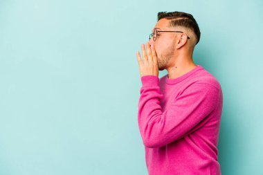 Genç İspanyol bir adam mavi arka planda izole edilmiş. Gördüğü bir şey yüzünden şok oluyor..