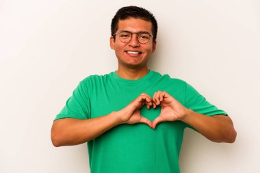 Beyaz arka planda izole edilmiş genç İspanyol adam gülümsüyor ve elleriyle kalp şeklini gösteriyor..