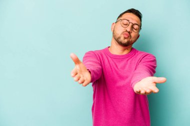 Genç İspanyol adam mavi arka planda izole edilmiş dudaklar kıvrılıyor ve hava öpücüğü göndermek için avuç içleri tutuyor..
