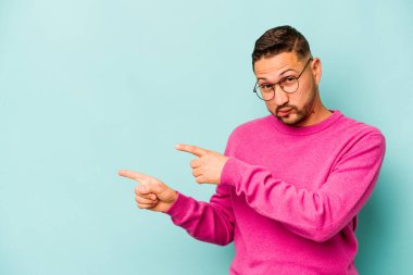 Mavi arka planda izole edilmiş genç İspanyol adam işaret parmaklarıyla fotokopi alanını işaret ederek heyecan ve arzuyu ifade ediyor..