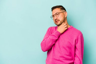 Genç İspanyol bir adam mavi arka planda izole edilmiş kafasının arkasına dokunuyor, düşünüyor ve bir seçim yapıyor..