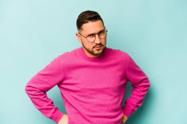 Mavi arka planda izole edilmiş, hoşnutsuzca kaşlarını çatmış, kollarını kavuşturmuş genç bir İspanyol..