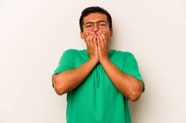 Beyaz arka planda izole edilmiş genç İspanyol bir adam bir şeye gülüyor, elleriyle ağzını kapatıyor..