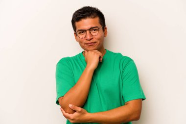 Beyaz arka planda izole olmuş genç İspanyol adam gülümsüyor ve kendinden emin, elleriyle çeneye dokunuyor..