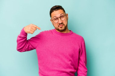 Mavi arka planda izole edilmiş genç bir İspanyol gömlek fotokopisini elle işaret ediyor, gururlu ve kendinden emin.