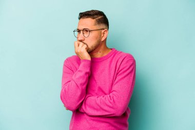 Mavi arka planda izole edilmiş, tırnak yiyen, gergin ve endişeli genç bir adam..