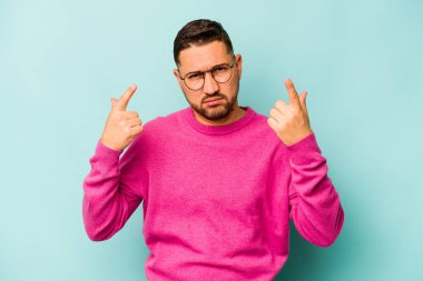 Mavi arka planda izole edilmiş genç İspanyol adam işaret parmağıyla bir hayal kırıklığı gösteriyor..