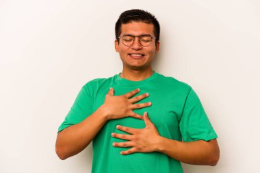 Beyaz arka planda izole edilmiş genç İspanyol adam mutlu bir şekilde gülüyor ve ellerini karnının üstünde tutarak eğleniyor..