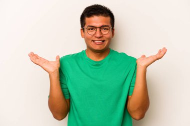 Beyaz arka planda izole edilmiş genç İspanyol adam kollarıyla ölçeği yapıyor, mutlu ve kendinden emin hissediyor..