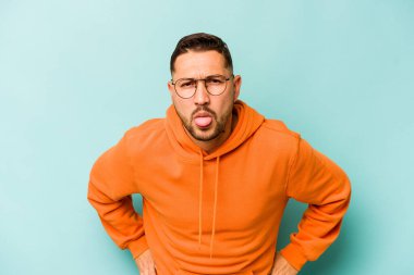 Genç İspanyol adam mavi arka planda izole edilmiş komik ve dost canlısı bir dil uzatıyor..