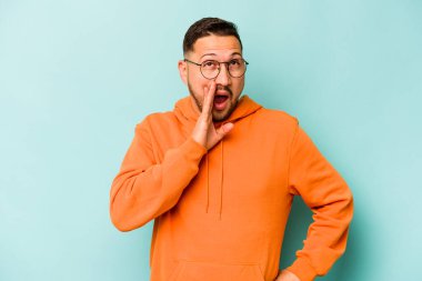 Genç İspanyol adam mavi arka planda izole edilmiş, heyecanlı bir şekilde bağırıyor..