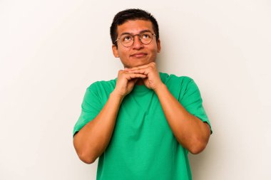 Beyaz arka planda izole edilmiş genç İspanyol adam ellerini çenesinin altında tutuyor ve mutlu bir şekilde yan tarafa bakıyor..