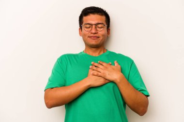 Beyaz arka planda izole olmuş genç İspanyol adam gülüyor, elleri yüreğinde, mutluluk kavramında..