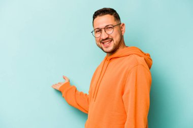 Mavi arka planda izole edilmiş genç bir İspanyol hoş geldin ifadesi sergiliyor..