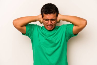 Latin kökenli genç adam beyaz arka planda izole edilmiş. Kulakları kulaklarıyla kapatıyor. Çok fazla ses duymamaya çalışıyor..