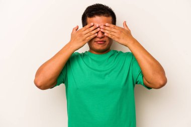 Beyaz arka planda izole edilmiş genç İspanyol adam elleriyle gözlerini kapatmaktan korkuyor..