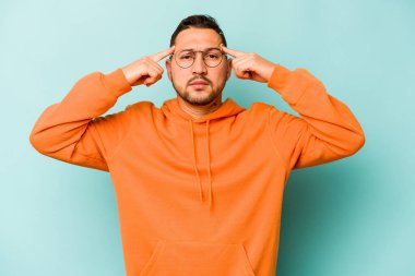 Mavi arka planda izole edilmiş genç İspanyol bir adam bir göreve odaklanmış, işaret parmaklarını işaret ediyor..