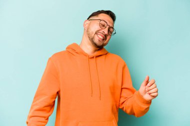 Genç İspanyol adam mavi arka planda izole edilmiş dans ediyor ve eğleniyor.