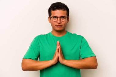 Latin kökenli genç bir adam beyaz arka planda izole edilmiş dua ediyor, bağlılık gösteriyor, dindar biri ilahi ilham arıyor..