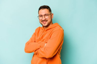 Mavi arka planda kendini güvende hisseden, kararlılıkla kollarını kavuşturan genç İspanyol bir adam..