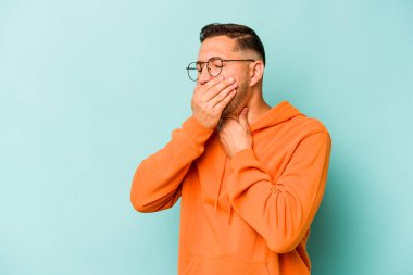 Mavi arka planda izole edilmiş genç İspanyol bir adam virüs ya da enfeksiyon yüzünden boğazında ağrı hissediyor..