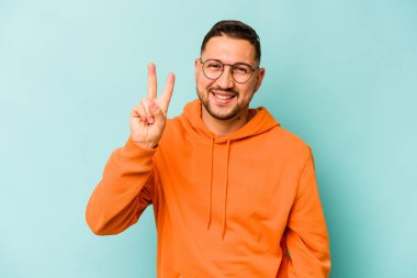Mavi arka planda izole edilmiş genç İspanyol adam iki numarayı parmaklarıyla gösteriyor..