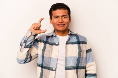 Beyaz arka planda izole edilmiş genç İspanyol adam işaret parmaklarıyla küçük bir şey tutuyor, gülümsüyor ve kendinden emin..