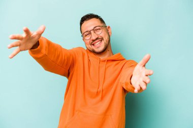 Mavi arka planda izole edilmiş genç İspanyol adam kameraya sarıldığı için kendinden emin hissediyor..