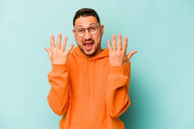 Mavi arka planda izole edilmiş genç İspanyol adam on numarayı elleriyle gösteriyor..