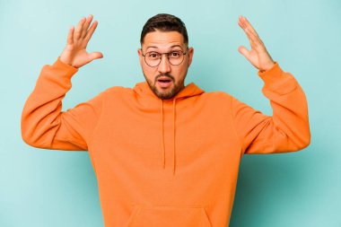 Latin kökenli genç bir adam mavi arka planda zaferi ya da başarıyı kutlarken şaşırmış ve şok olmuştu..