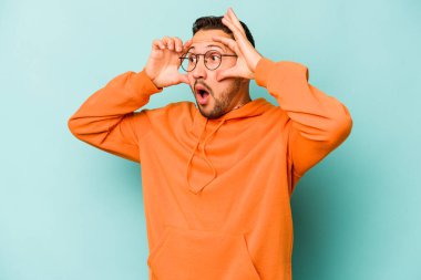 Genç İspanyol bir adam mavi arka planda izole edilmiş. Başarı fırsatı bulmak için gözlerini açık tutuyor..