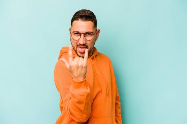 Mavi arka planda izole edilmiş genç İspanyol adam parmaklarıyla kaya hareketi gösteriyor.