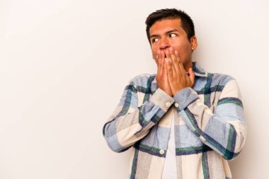 Genç İspanyol bir adam beyaz arka planda izole edilmiş. Düşünceli bir şekilde bir fotokopi odasına bakıyor. Ağzını eliyle kapatıyor..