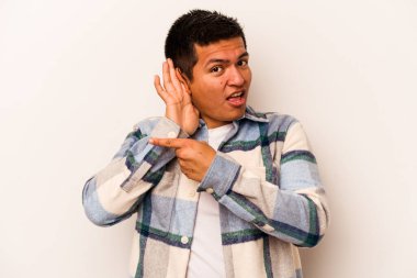 Latin kökenli genç bir adam beyaz arka planda bir dedikoduyu dinlemeye çalışıyor..