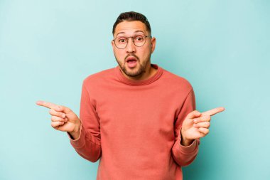 Mavi arka planda izole edilmiş genç İspanyol adam farklı kopya alanlarını gösteriyor, birini seçiyor, parmaklarıyla gösteriyor..